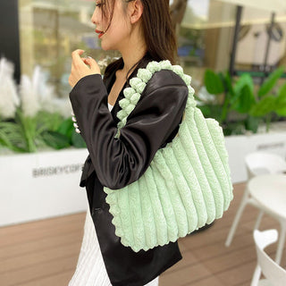 Stylish plush mint green tote bag with textured pattern, held by a woman in a black dress against a natural backdrop.