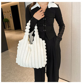 Stylish black and white plush handbag with unique design details, carried by a person in a formal black outfit, standing in an interior setting.
