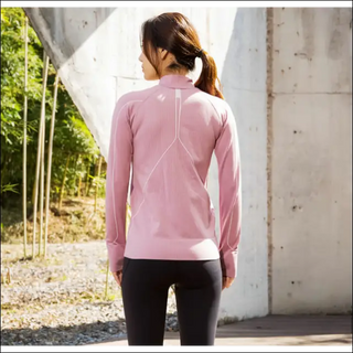 Slim fit sports jacket in soft pink color, showcased on a woman standing in an outdoor setting with a concrete wall and nature elements in the background.