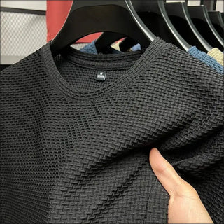 Textured black mesh t-shirt from the K-AROLE fashion brand, displayed on a clothing rack in a store setting.