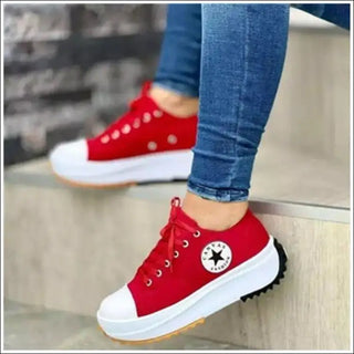 Vibrant red canvas sneakers with white soles, lace-up closure, and signature star logo on the side, worn with blue denim jeans in a casual, stylish setting.