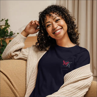 Radiant woman with curly hair wearing cozy beige sweater and navy t-shirt with embroidered design, smiling happily while sitting on a sofa.