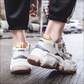 Stylish women's sneakers with chunky soles, featuring a white and gray color scheme with textured details. The sneakers are shown in an urban setting, with the wearer's legs and feet visible.