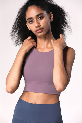 Supportive cross-back athletic bra top in purple, worn by female model with curly hair against white background.