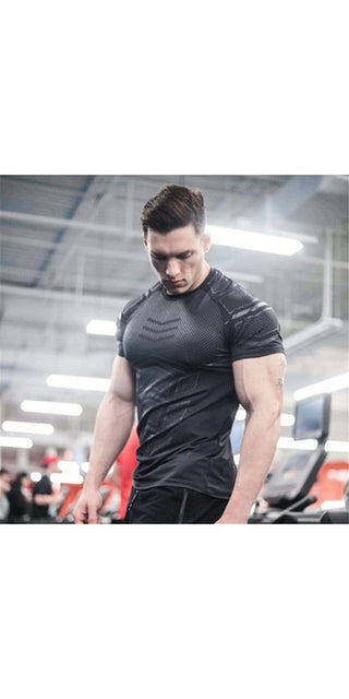 Muscular male model wearing a fitted black compression t-shirt in a fitness studio.