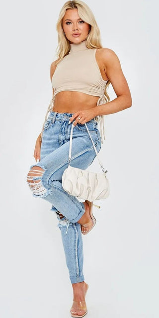 Stylish cropped beige top with side-tie detail, worn with distressed blue jeans and a white shoulder bag, creating a trendy casual outfit.