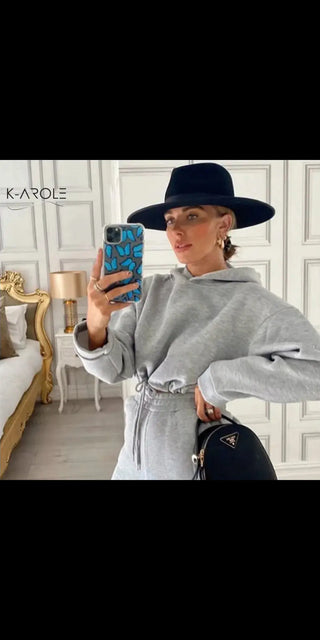 Stylish K-AROLE™️ woman in gray sweatsuit taking a selfie with her smartphone in a luxurious indoor setting.
