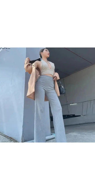 Stylish woman wearing light gray two-piece outfit consisting of slim-fit long pants and matching cropped top, standing confidently in a modern urban setting.