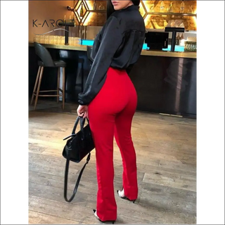 Fashionable woman wearing bold red pants and a casual black jacket, posing in front of a stylish café interior.