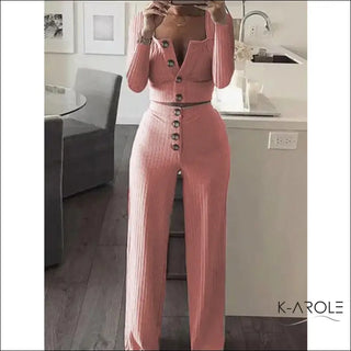 Stylish pink knitted women's long sleeve set with button-up top and high-waisted pants from fashion brand FashionExpress, displayed on a wooden table in front of framed artwork.